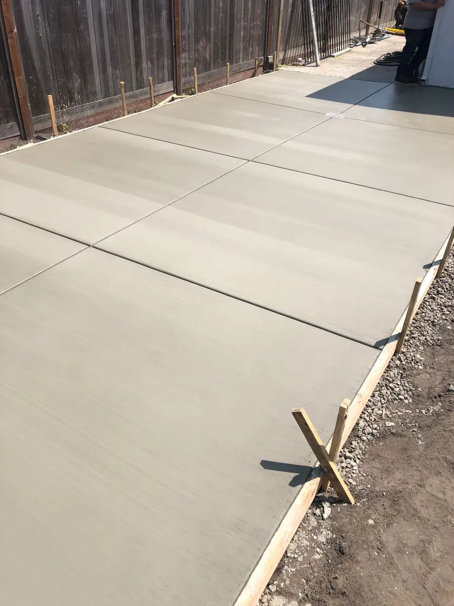 Finished broom-finish concrete patio with control joints along a fence.