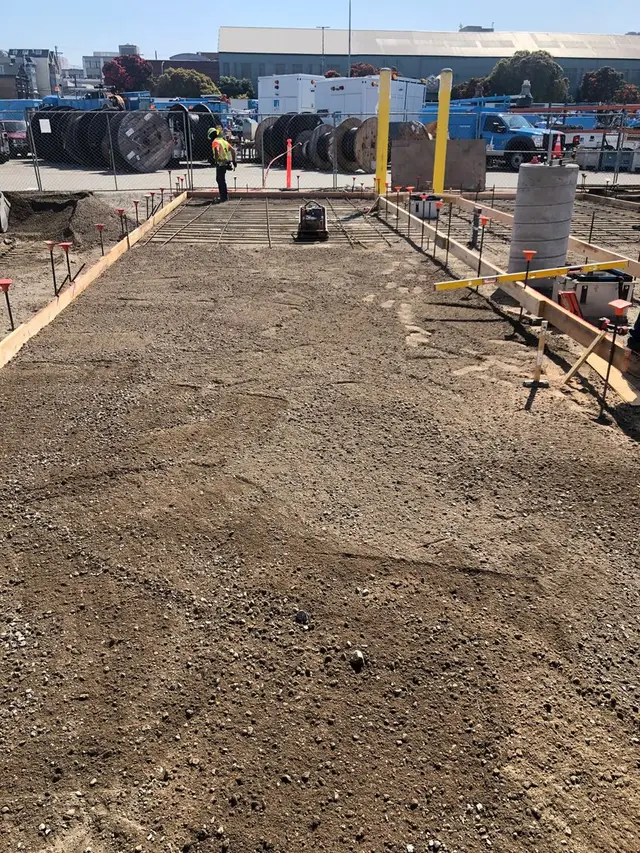 Graded and compacted base with forms and stakes set along the edge of a slab.
