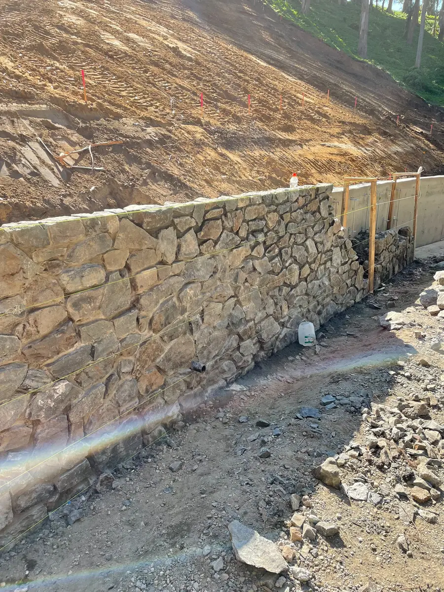 Natural stone retaining wall built into a graded slope with drainage rock at the base.